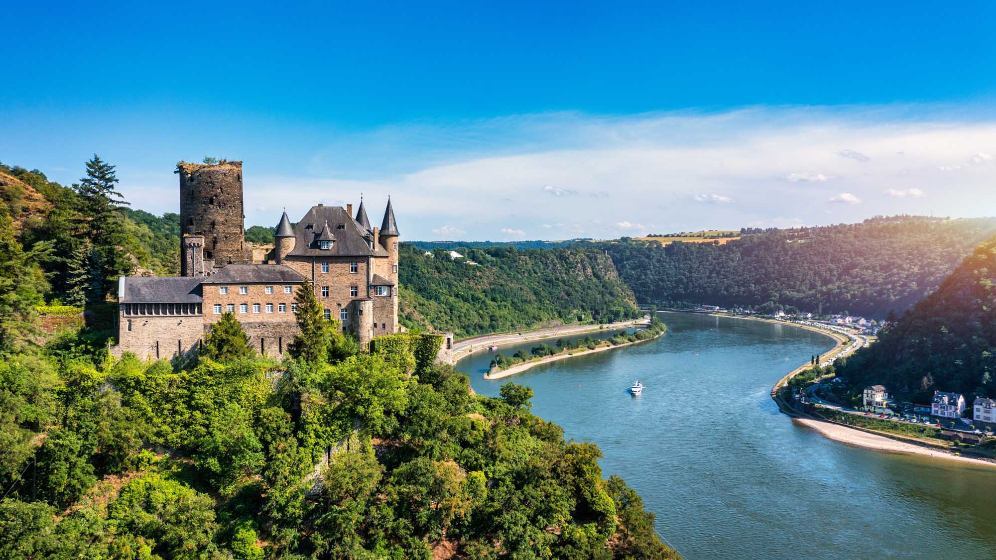 A picturesque medieval castle perched dramatically on a forested cliff overlooking a sweeping bend