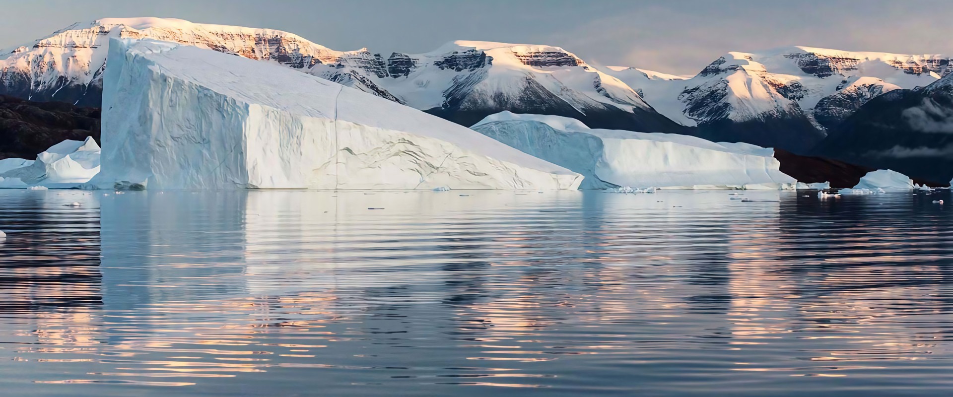 Massive tabular icebergs floating in calm Arctic waters with snow-capped mountains