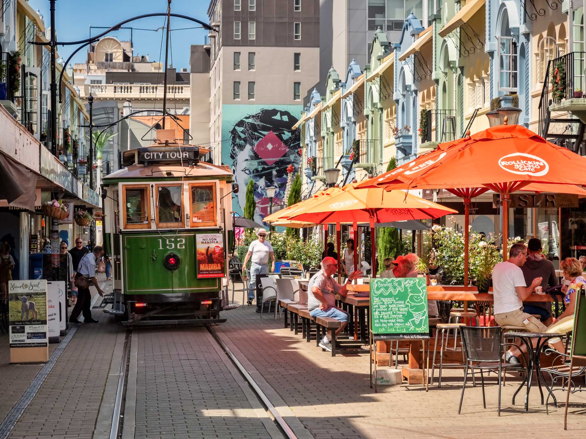 Vibrant outdoor cafés line Christchurch's historic New Regent Street with red umbrellas and a vintage tram