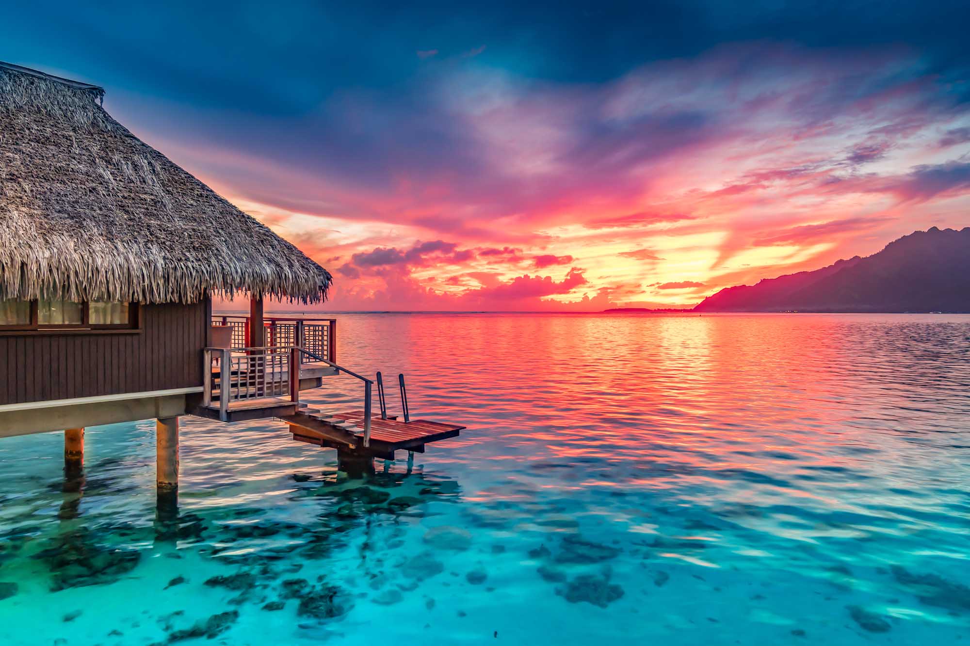 Overwater bungalow with thatched roof at sunset in Moorea, French Polynesia