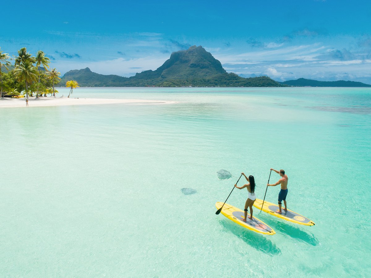 Two paddleboarders navigate the crystal-clear turquoise lagoon of Bora Bora with the iconic