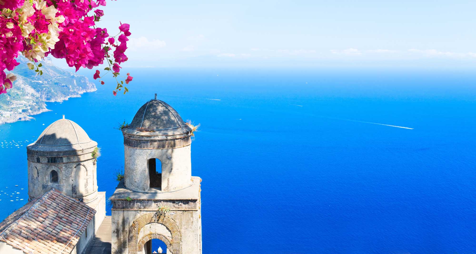 Two iconic white stone belltowers with dome caps overlook the brilliant blue Mediterranean Sea from
