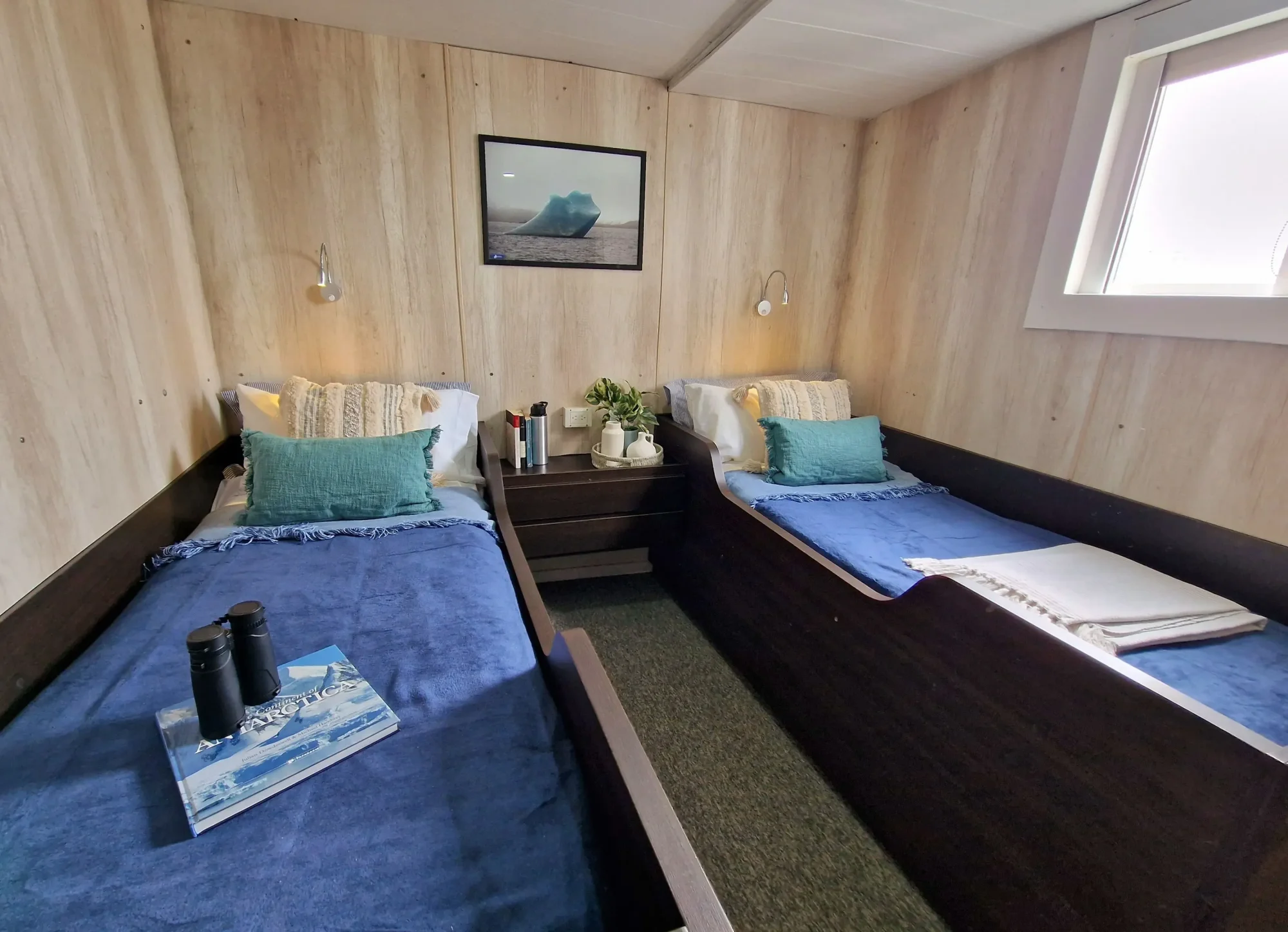 Compact twin-bed cabin with light wood paneling aboard an Antarctic expedition vessel