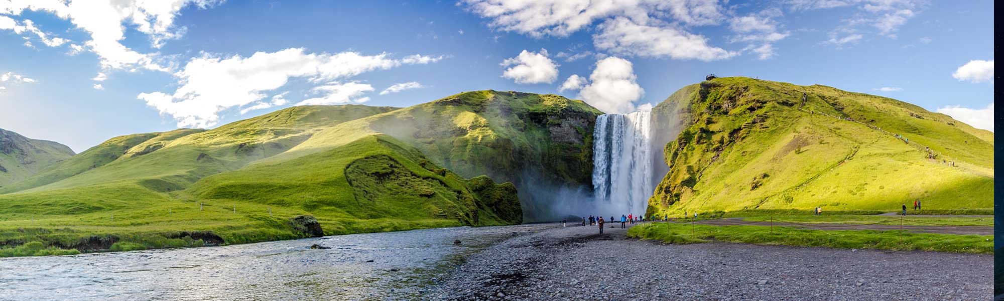 Skógafoss Waterfall cascades down moss-covered cliffs into a glacial river in Iceland