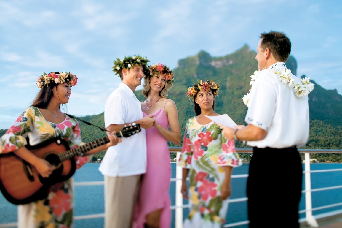 Wedding party in tropical attire celebrates on cruise ship deck with volcanic island backdrop