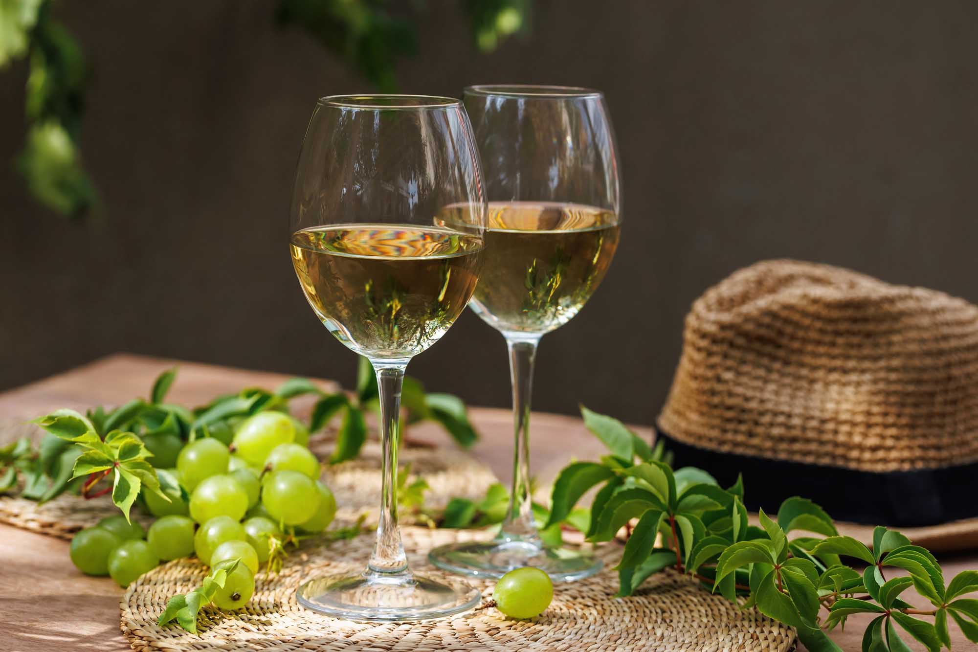 Two glasses of crisp white wine are elegantly arranged on a wooden table alongside fresh green