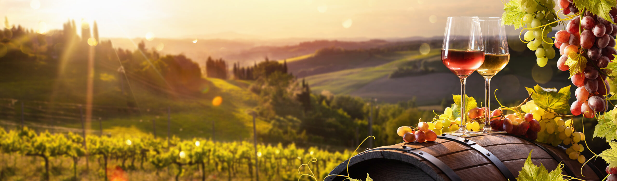 Two wine glasses on a barrel overlooking rolling Tuscan vineyards at golden sunset