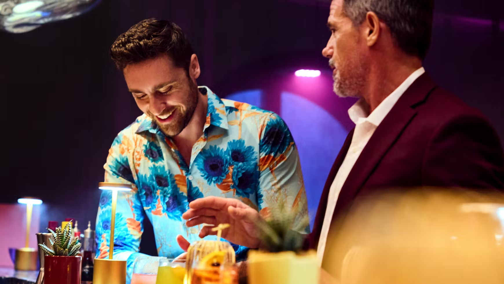 Adult Guests Socializing at Virgin Voyages Bar Two well-dressed adult guests enjoy cocktails and conversation at an elegant bar venue aboard