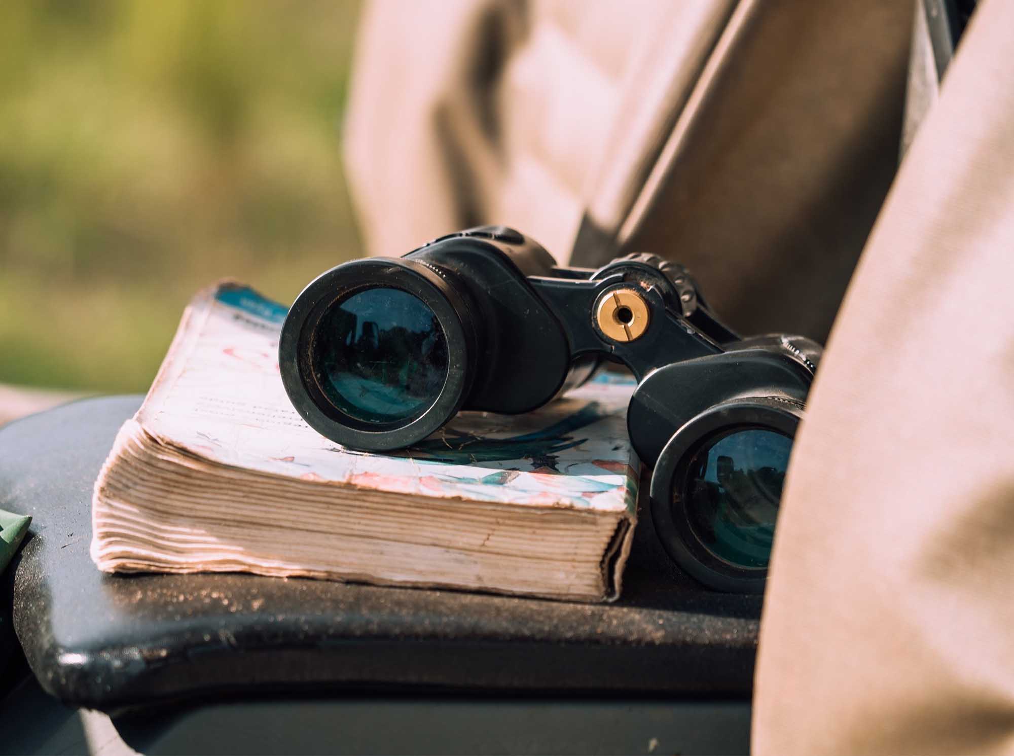 A close-up of black binoculars resting on an open vintage map, held by someone in outdoor clothing
