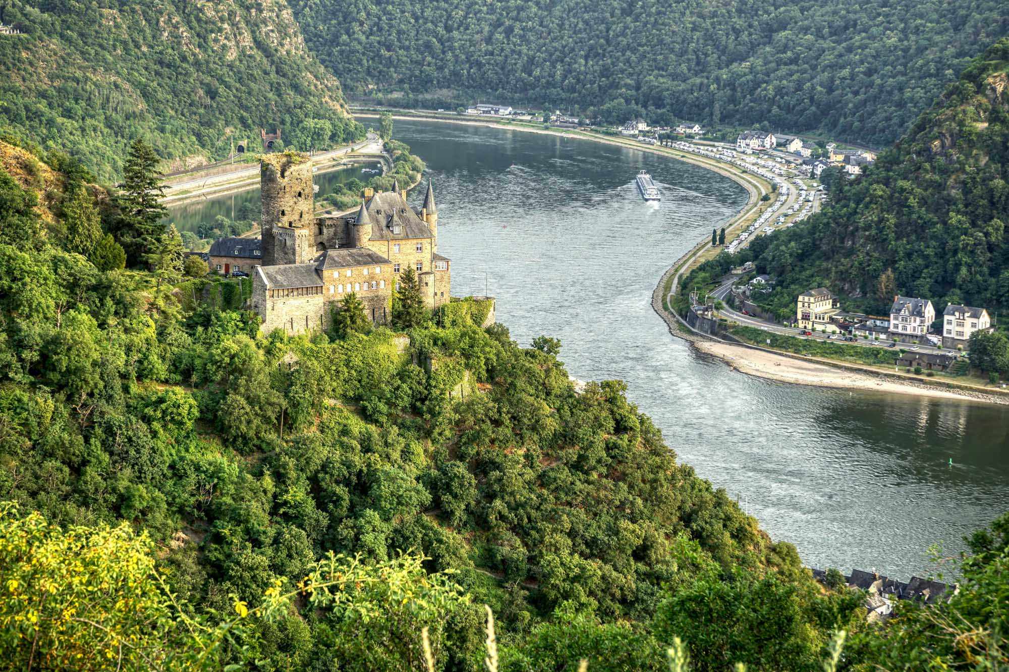 A stunning aerial view of a medieval castle perched on a forested cliff overlooking a meandering