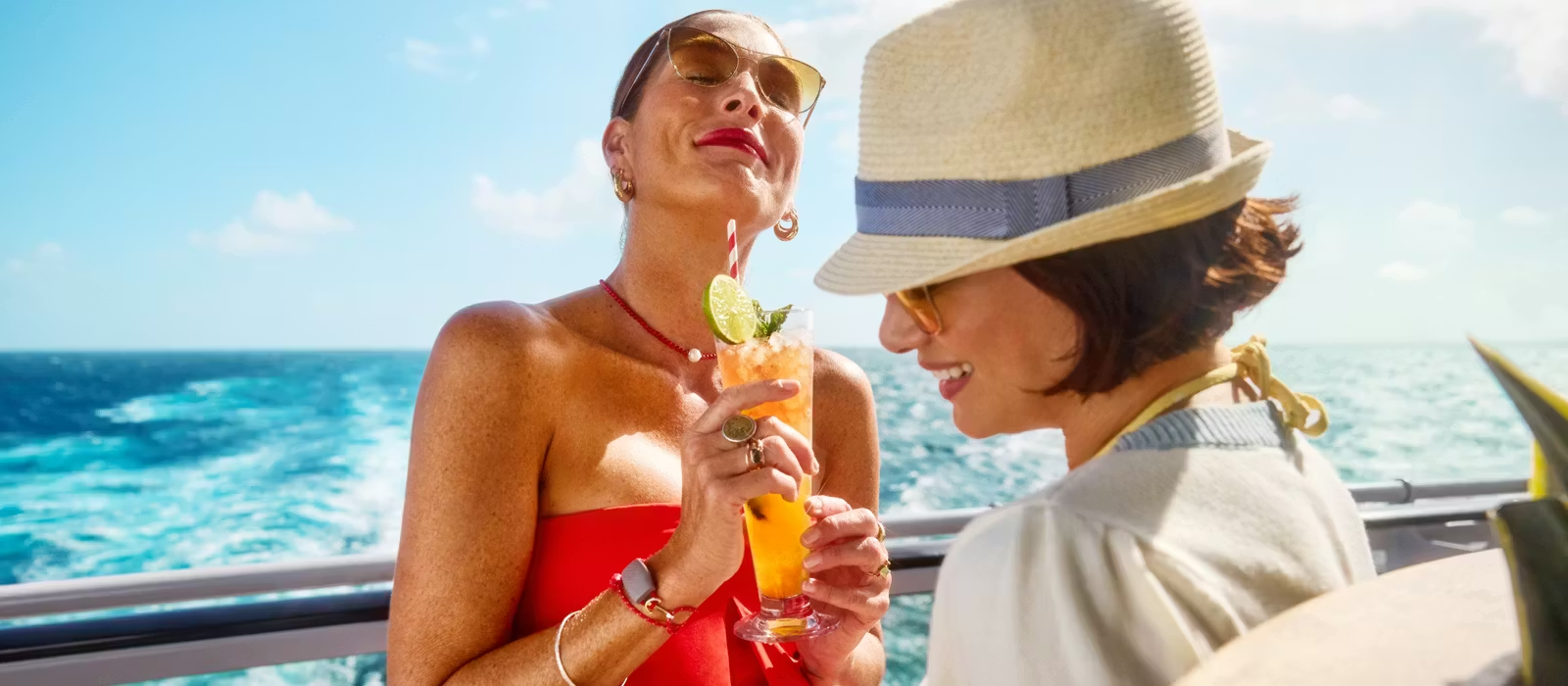 Cocktails on Virgin Voyages Brilliant Lady Deck Two women enjoy tropical cocktails on the deck of Virgin Voyages' Brilliant Lady, with sparkling