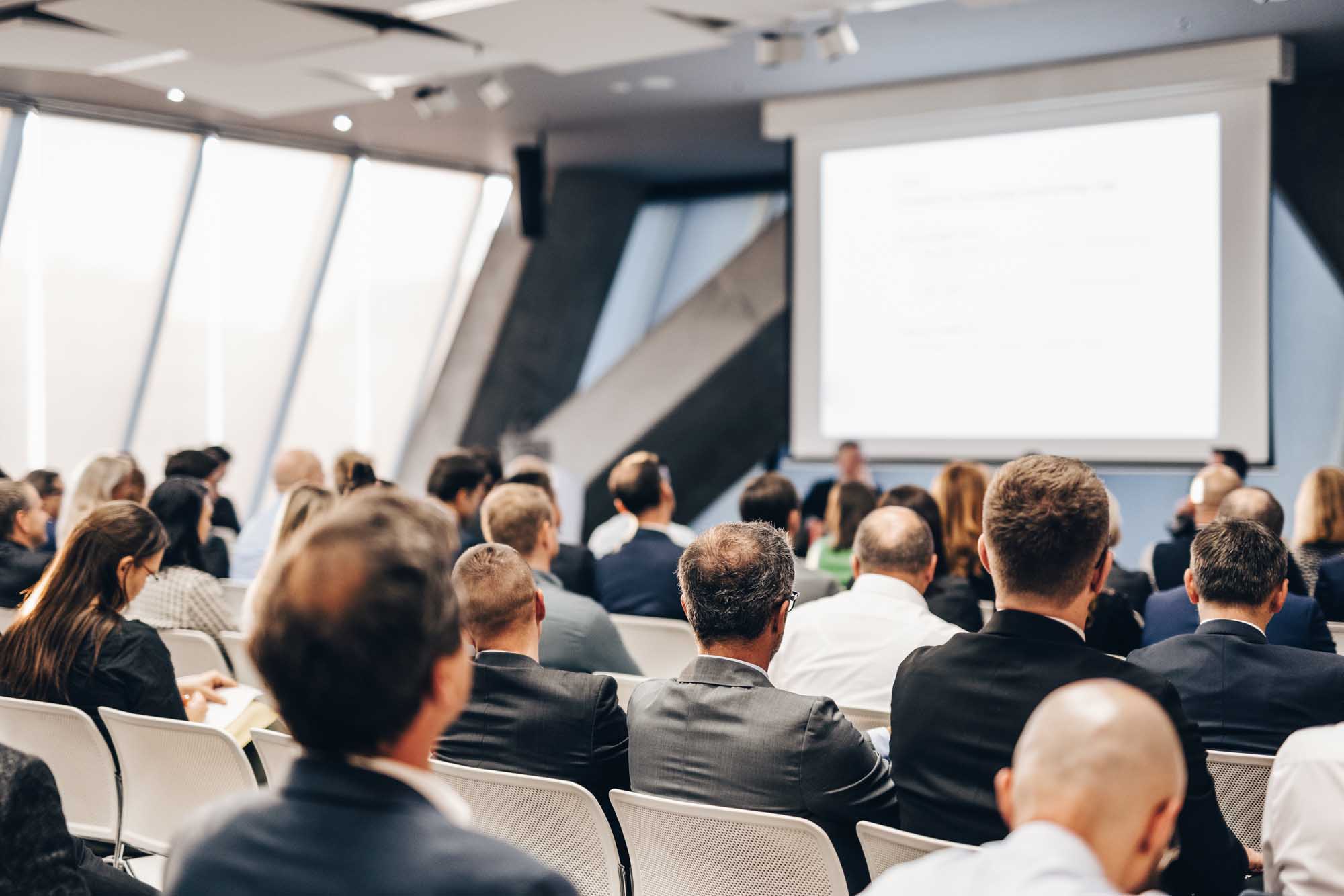 A large audience of business professionals seated in a modern conference hall attending a corporate