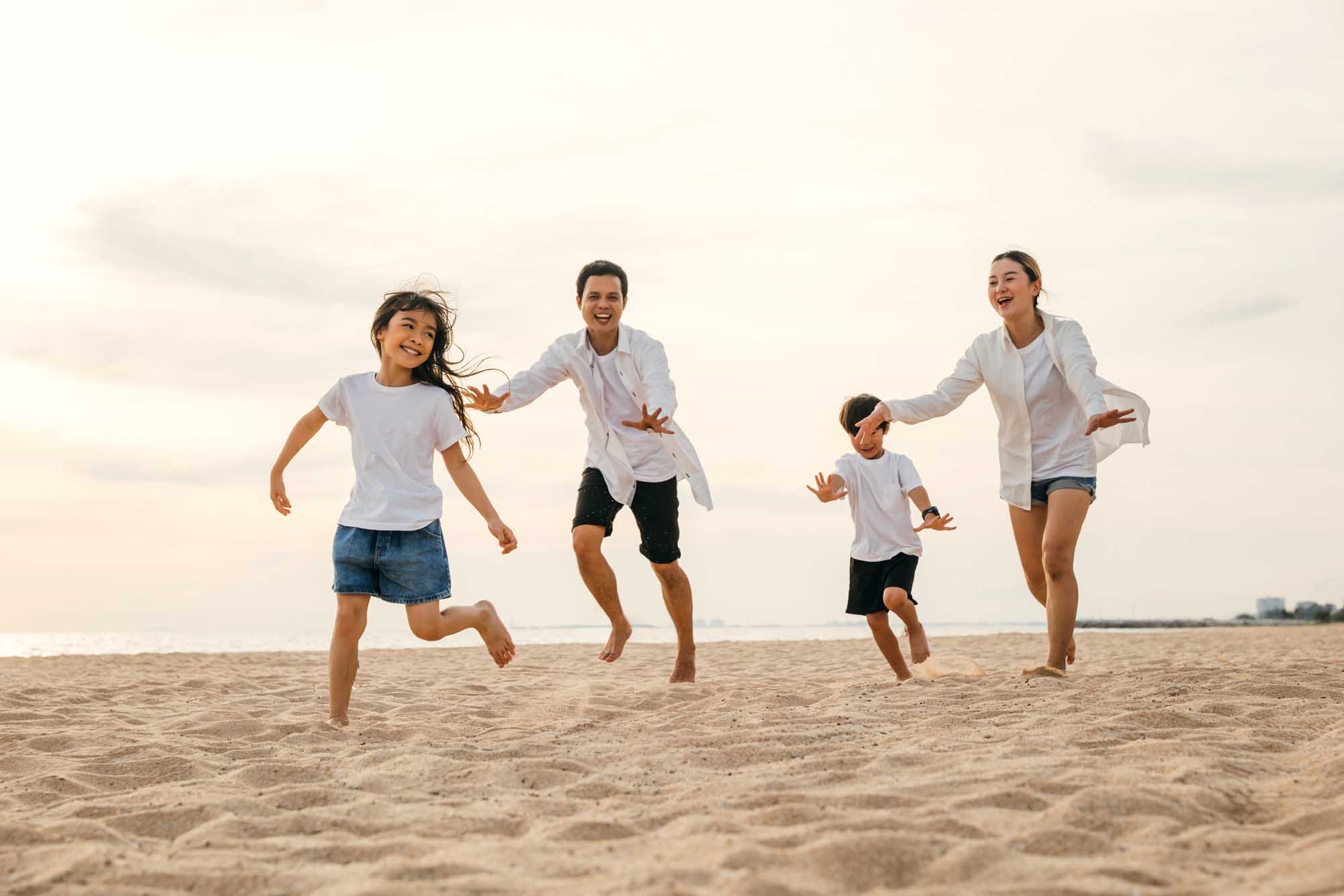 Happy Family Running on Beach at Sunset A cheerful family of five enjoys a carefree moment running barefoot along a sandy beach at golden