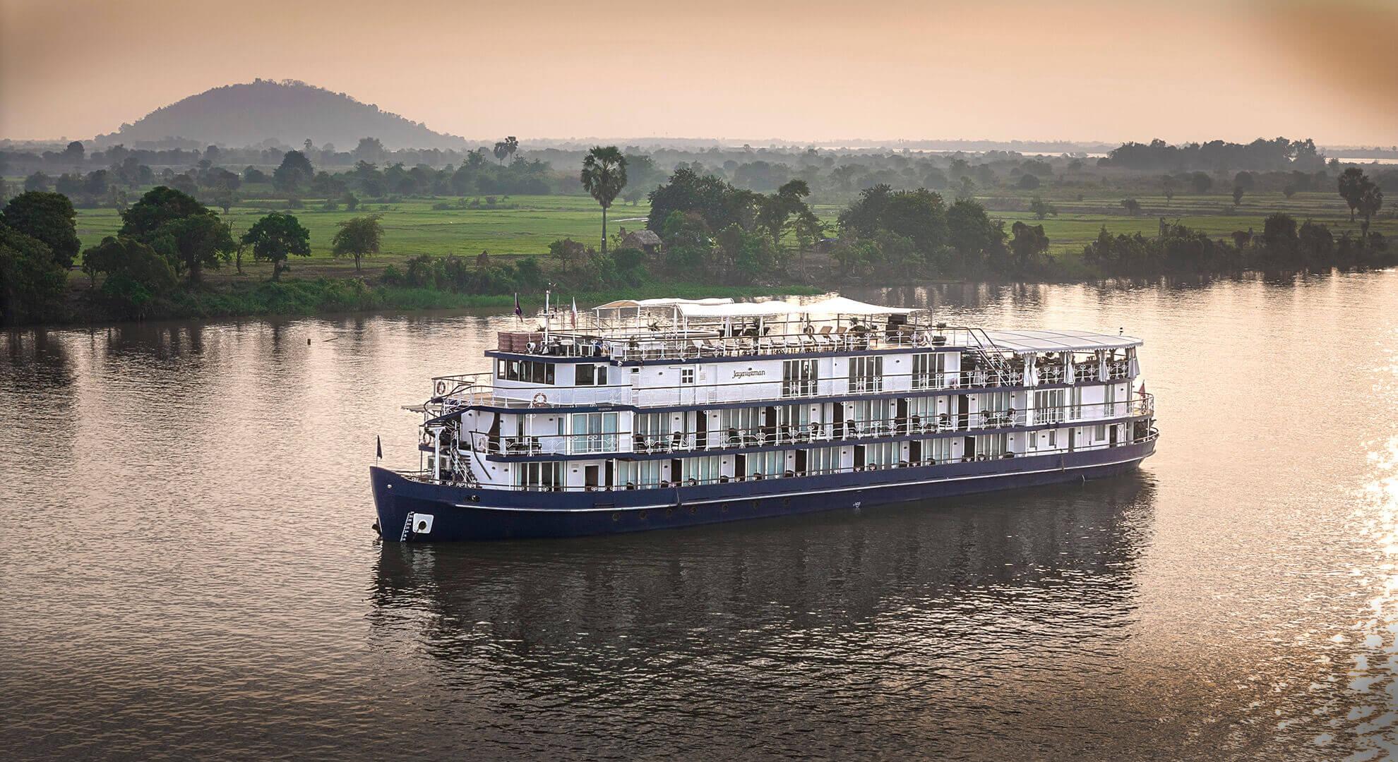 A luxurious river cruise ship, the Jayavarman, navigates the serene Mekong River with verdant