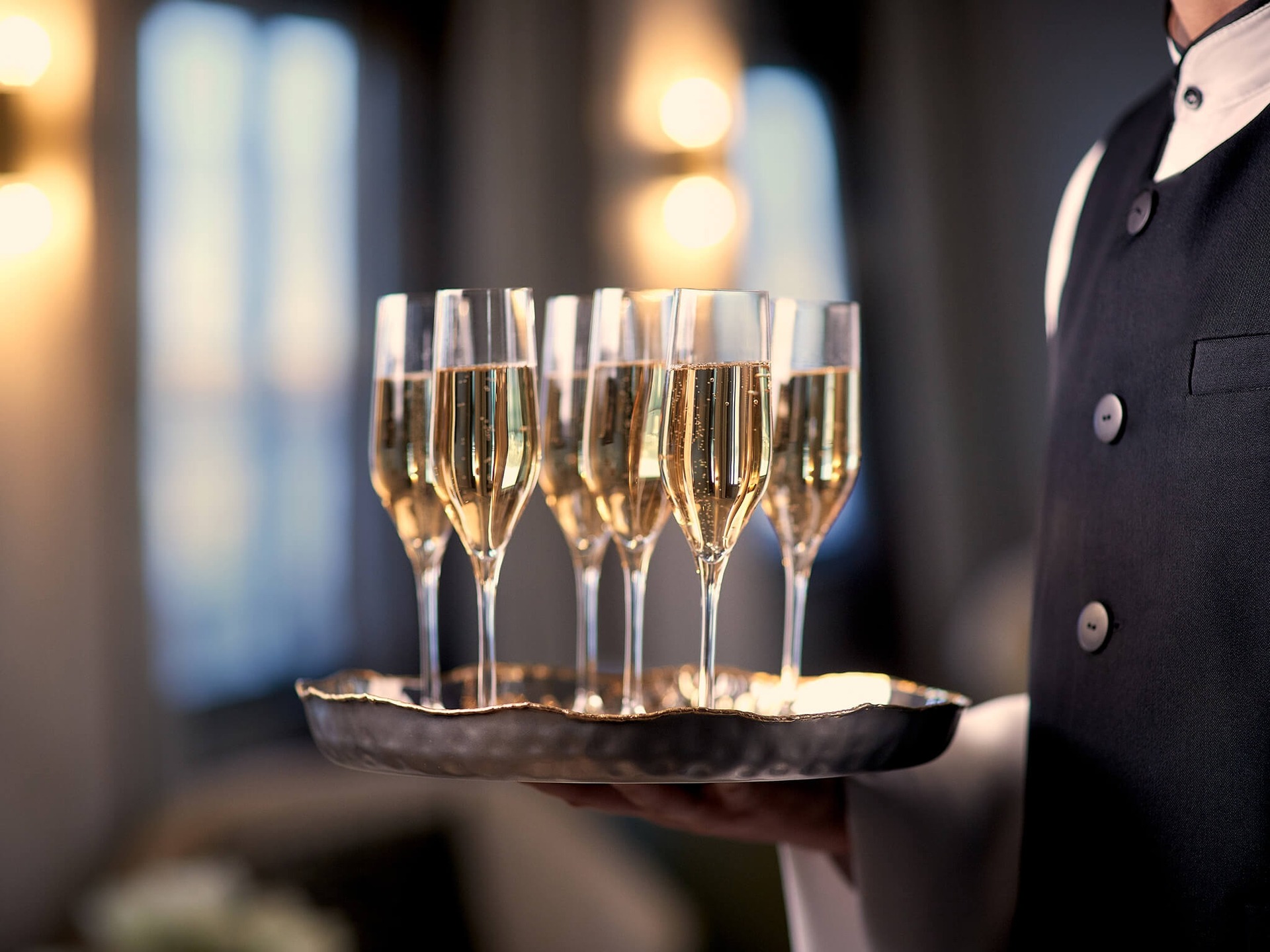 A professionally dressed server presents an elegant tray of champagne flutes filled with sparkling