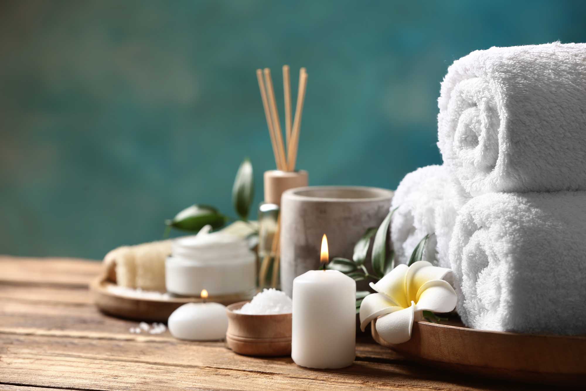A serene spa and wellness arrangement featuring rolled white towels, lit candles, plumeria flowers