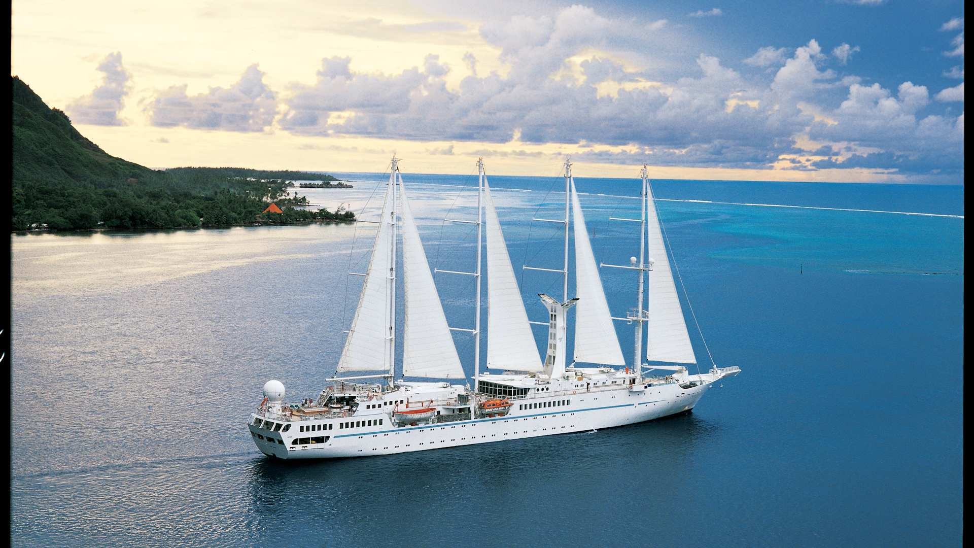 Windstar Cruises Sailing Vessel in Tropical Waters A luxurious four-masted sailing cruise ship with white sails fully deployed, anchored