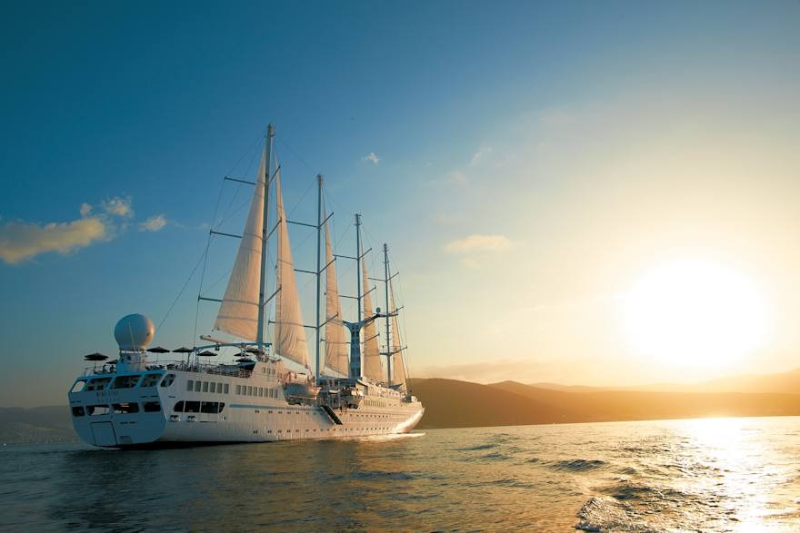 Windstar Cruises Wind Spirit at Sunset A luxury small-ship cruise vessel with four tall masts and white sails unfurled, anchored in calm