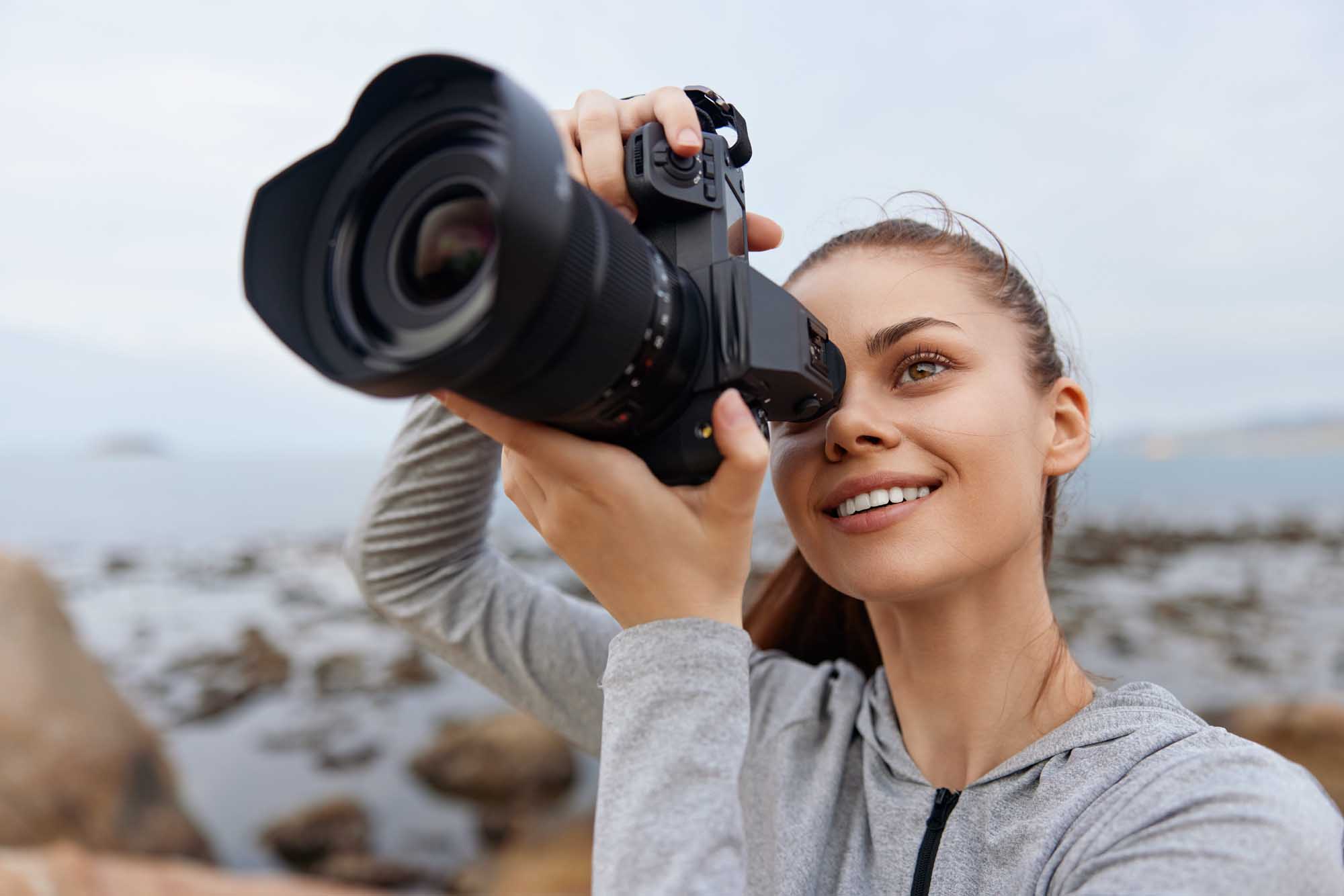 A young female photographer smiles while holding a professional DSLR camera with telephoto lens